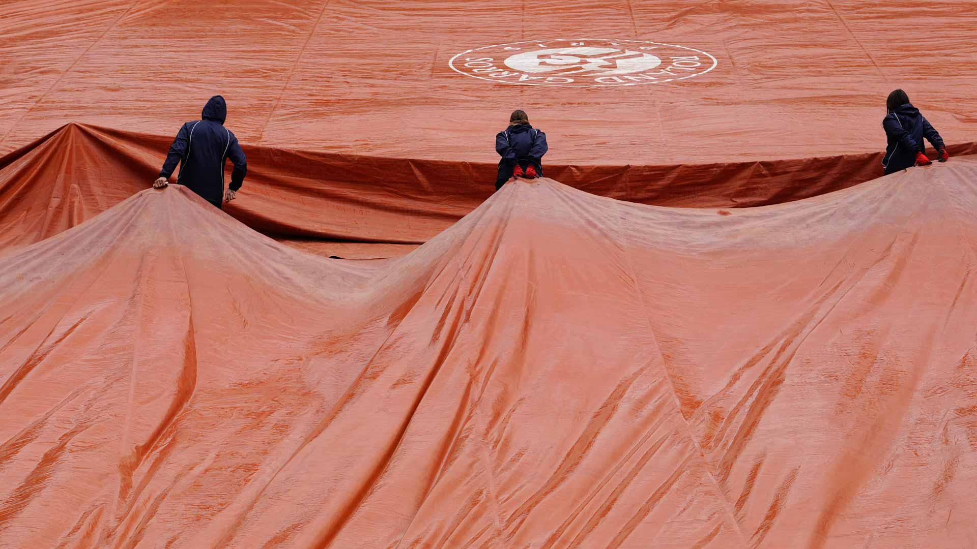 Tournament staff covers a court at Roland Garros due to Friday rain.