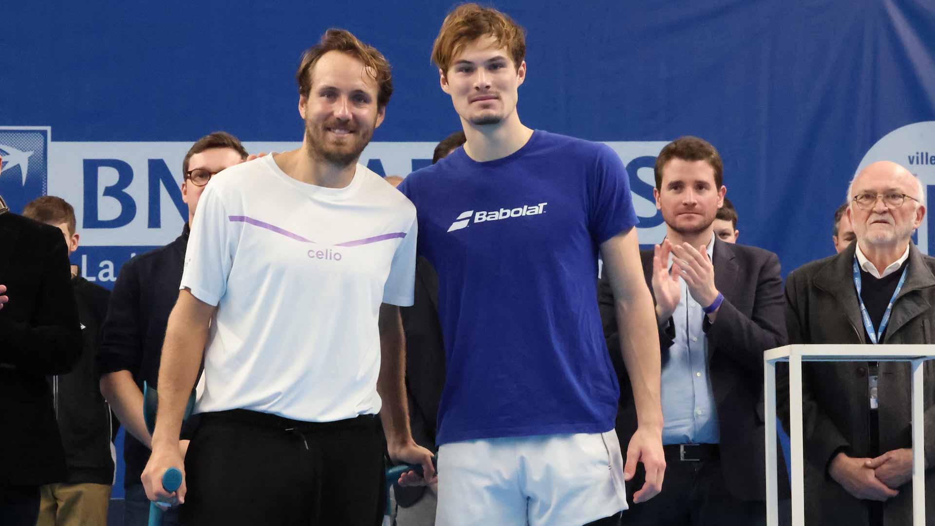 On crutches during the trophy ceremony, <a href='https://www.atptour.com/en/players/lucas-pouille/pf39/overview'>Lucas Pouille</a> (left) poses next to <a href='https://www.atptour.com/en/players/arthur-bouquier/b0er/overview'>Arthur Bouquier</a>.