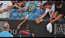Nick Kyrgios signs a racquet he had given to a fan during the first set of his double quarter-final win with Thanasi Kokkinakis at the Australian Open.