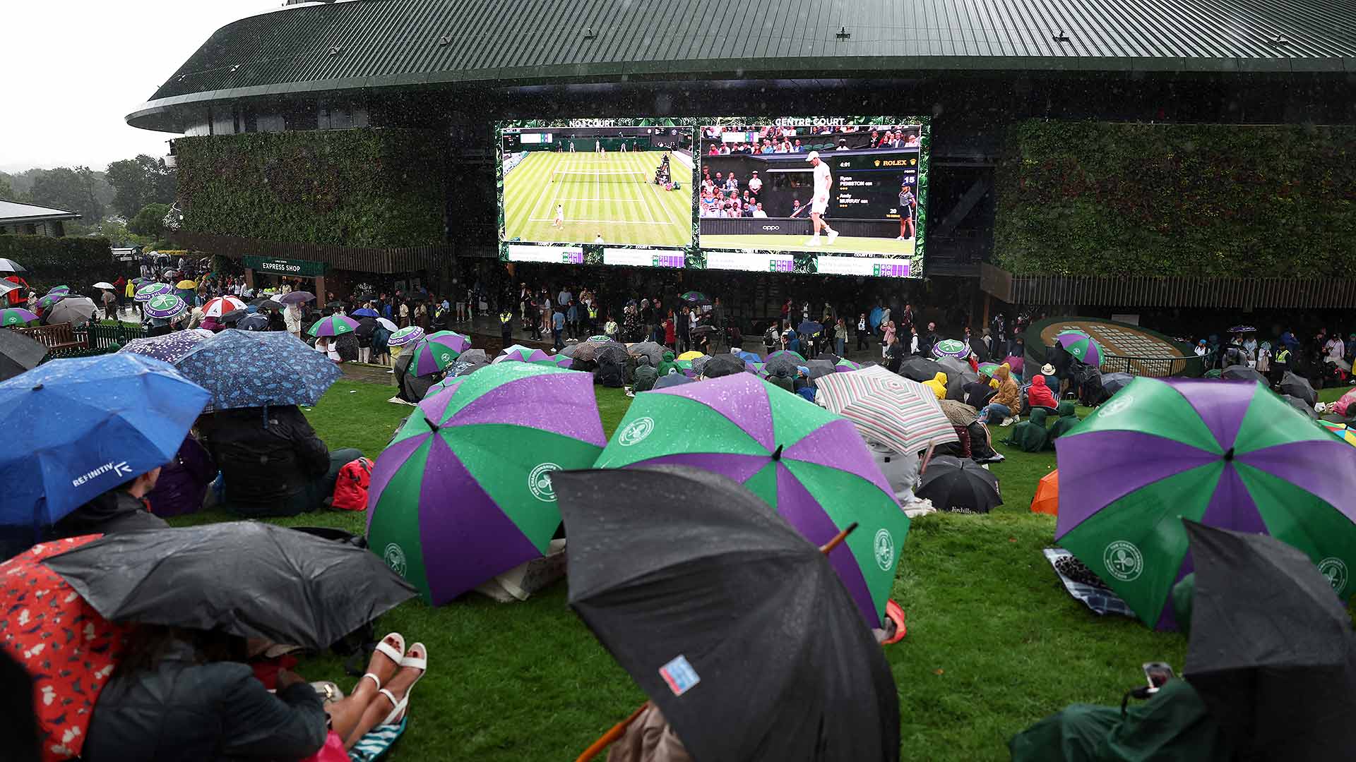 Fans on Henman Hill battle to keep dry while watching Andy Murray take on Ryan Peniston under a closed Centre Court roof on Day 2.