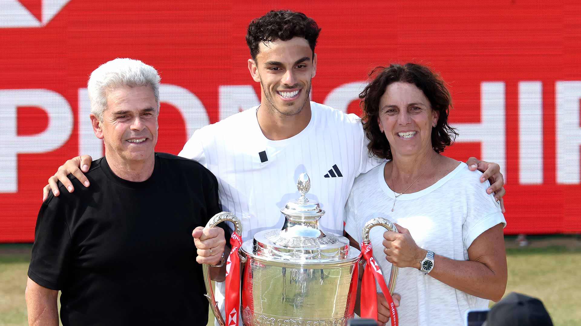 Francisco Cerundolo lifts the Queen's Club trophy in London with father Alejandro and mother Maria Luz.